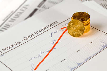 Gold Eagle one ounce coins stacked into graph of gold prices on business pages of newspaper with graphs showing increase in valueの写真素材