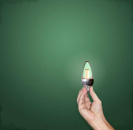 Hand holding a bright LED lightbulb in front of a green chalkboard with plenty of copy space