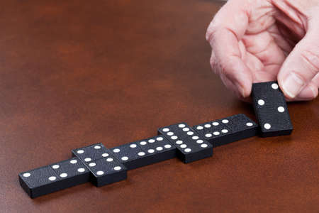 Macro image of dominos on a leather table in the middle of a game with hand placing a tile