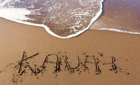Kauai written in sand on beach with sea waves starting to erase the word