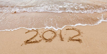 2012 written in sand on beach with sea waves starting to erase the wordの写真素材
