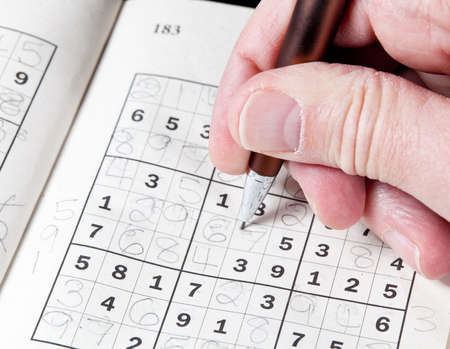 Male hand holding pen or pencil on suduko puzzleの写真素材