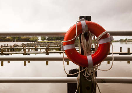 Lone red life ring and rope in front of empty boat docks on a cloudy rainy day with no boatsの写真素材