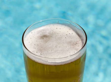 Plain pint glass of cold lager beer sitting on edge of blue swimming poolの写真素材