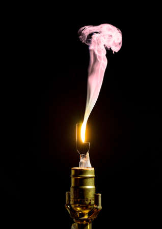 Filament on broken incandescent light bulb flares and gives off smokeの写真素材