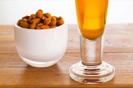 Raw almond nuts in white glass bowl on old wooden table with glass of cold beerの写真素材