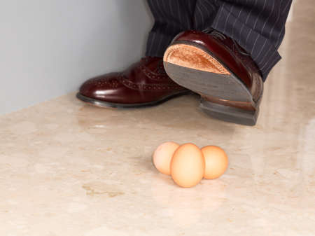 Male brown leather shoe in suit pants about to tread on three brown eggsの写真素材