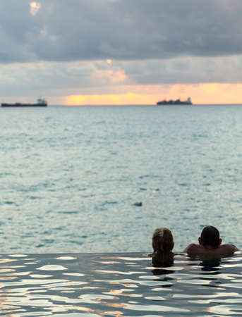 Silhouette of couple heads at the edge of infinity swimming pool overlooking ocean at sunsetの写真素材
