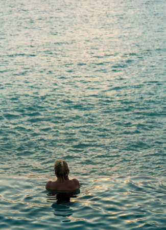 Silhouette of person head at the edge of infinity swimming pool overlooking ocean at sunsetの写真素材
