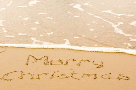 Merry Christmas sign written in sand on beach with waves approaching