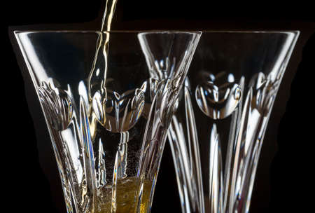 Detail of a pair of cut glass champagne goblet with a heart on the side and drink being pouredの写真素材