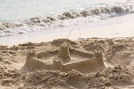 Sandcastle built in sand by sloping sandy beach to surf by oceanの写真素材