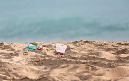 Discarded childs flip flops on sandy beach by turquoise ocean in sun