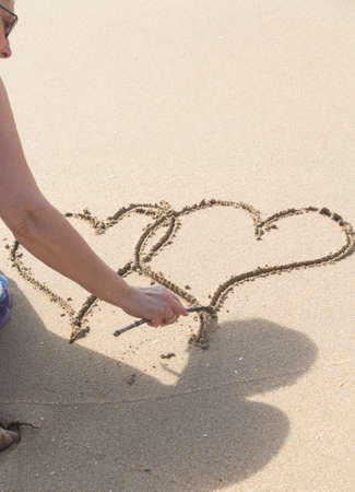 Lady drawing pair of linked hearts in sand on beach in Caribbeanの写真素材