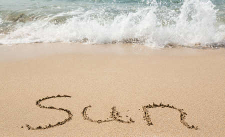 Sand drawing on warm beach by ocean surf in Caribbean spelling Sunの写真素材