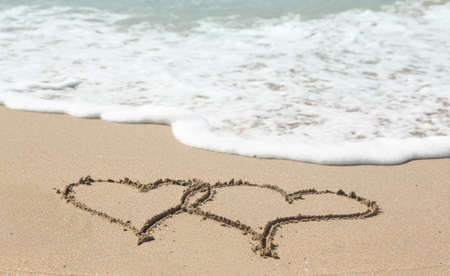 Sand drawing on warm beach by ocean surf in Caribbean with linked heartsの写真素材