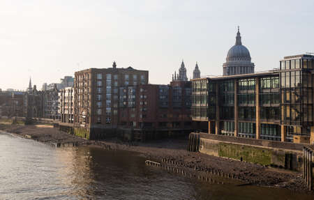 Modern apartments and homes by river Thames with St Pauls Cathedral in London England at dusk as the sun is setting low in sky.の写真素材