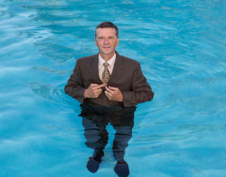 Senior caucasian businessman in suit up to waist in deep blue water and smiling at the cameraの写真素材