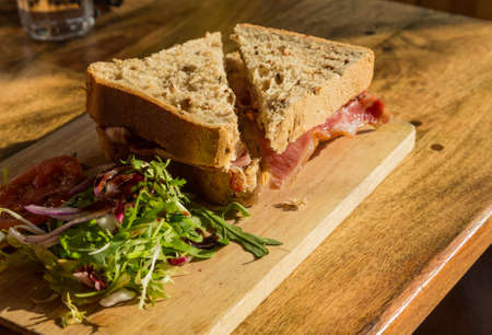 Bacon sandwich on thick wholemeal granary bread on wooden platter on pub lunch tableの写真素材