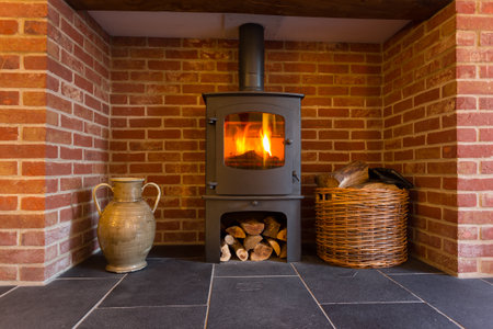 Roaring fire inside wood burning stove in brick fireplace with basket of cut wood ready for burningのeditorial素材