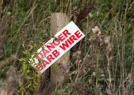 Danger barb or barbed wire sign nailed to post in heavily overgrown field or meadowの写真素材