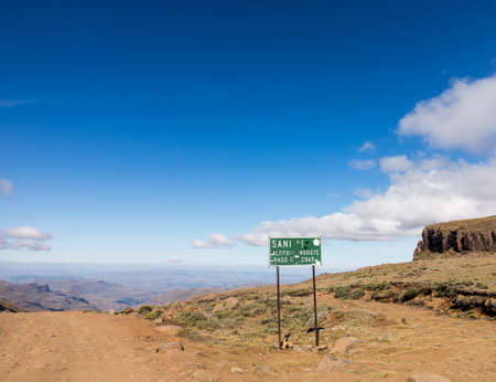 Sign post at summit with view of valley and winding road over mountains from South Africa to Lesotho over Sani Passの写真素材