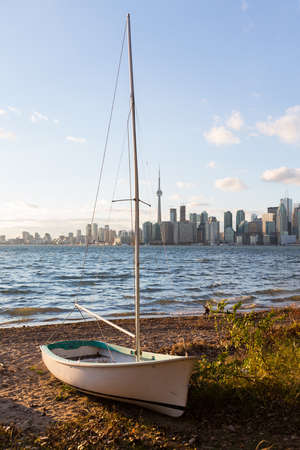 Single sailing boat beached on sandy shore of Lake Ontario on Wade Island of Toronto Islands with skyline の写真素材
