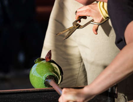 Glass blower artists work on adding decoration to ornate green glass bottle or bowlの写真素材