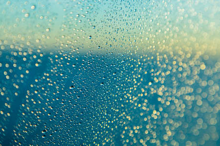 Blue color of ocean behind rain or spray drops on window of cruise ship as the sun starts to rise at...