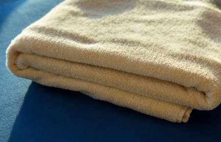 Folded stack of yellow bath or beach towels with the sun shining on the pile from the side giving a...