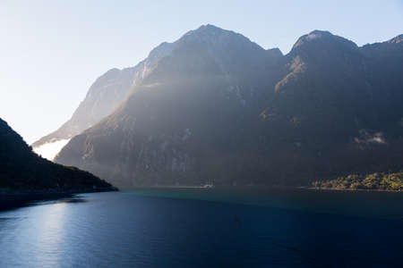 Sailing into Milford Sound on South Island of New Zealand in early morning as the sun rises above the mountainsの写真素材