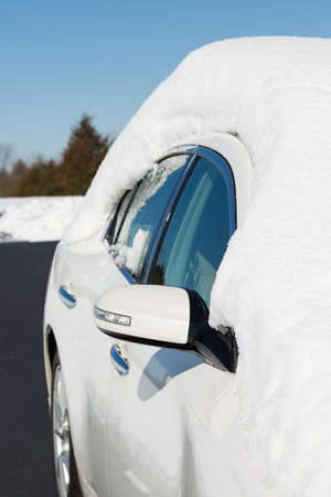 Deep snow piled high on top of white four door sedan car in rural setting with view down side of car and driveの写真素材