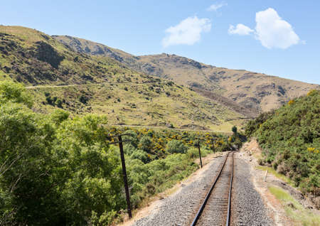 Railway track of Taieri Gorge tourist railway passes zigzag road on its journey up the valleyの写真素材
