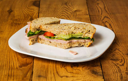 English ham lettuce and tomato sandwich with a bite out of one corner. Bread is artisan multigrain...