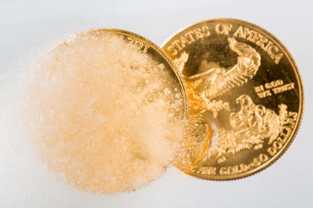 Gold eagle one ounce coin emerging from a frozen ice block to illustrate concept of gold coming out of deep freeze and price going to riseの写真素材