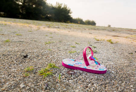 Concept image of the threat for child kidnapping or Amber alert with a single toddlers sandal alone on large beach with no sign of anyoneの写真素材