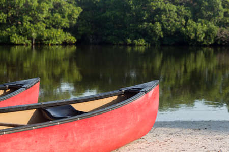Two red prows of canoes or kayaks with an open pond or river beach in background ready for paddling expeditionの写真素材
