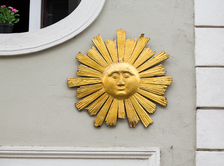Gold colored wooden carving of the face of the sun with rays and sunburst on wall in the medieval town of Regensburg, Bavaria, Germanyのeditorial素材