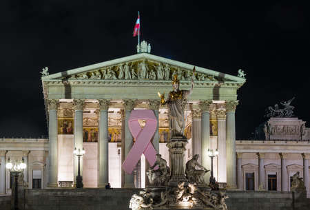 Illuminated facade of Austrian Parliament building with pink cancer ribbon in Vienna, Austriaの写真素材