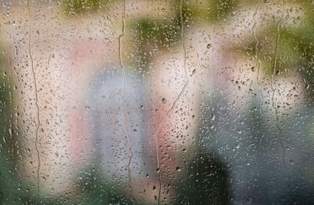 Colors of buildings and trees behind rain or spray drops on window of coachの写真素材
