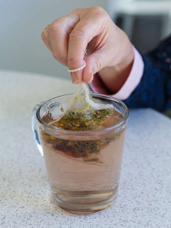 Lady hand dunking camomile or chamomile teabag in glass mug on cafe tableの写真素材