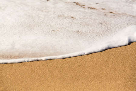 Ocean surf smoothly crossing the warm sand in white foam and bubbles as the waves race onto the...