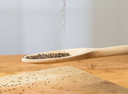 Superfood known as black chia seeds are poured into a wooden backing spoon over wood bread board on kitchen tableの写真素材