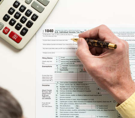 Male caucasian hand holding pen above USA tax form 1040 for year 2014  and calculator illustrating...