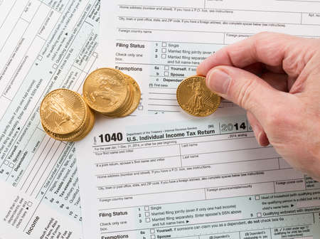 Caucasian hand counting solid gold eagle coins on USA tax form 1040 for year 2014 illustrating...