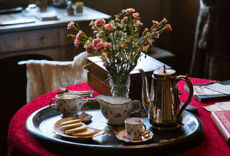Antique china tea cup and pot on silver tray with flowers on red tablecloth in old drawing roomの写真素材