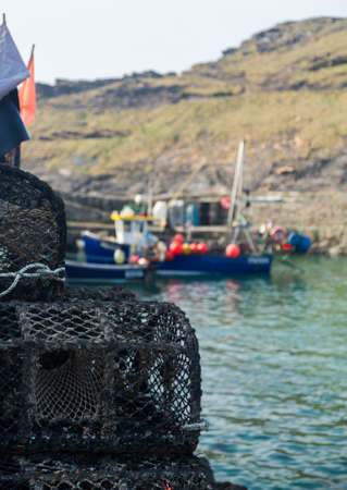 Rope and wooden frame lobster pot or trap stacked on stone wall of harbor in Boscastle, Cornwall, England UKの写真素材