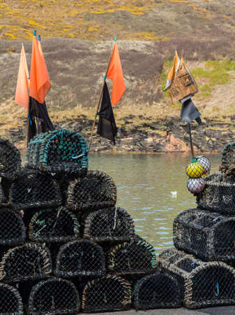 Rope and wooden frame lobster pot or trap stacked on stone wall of harbor in Boscastle, Cornwall, England UKの写真素材