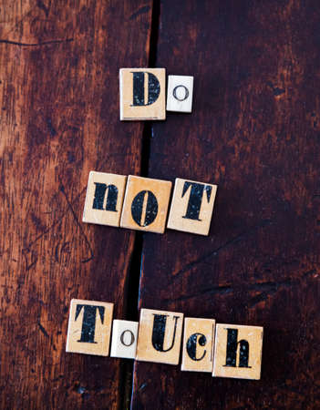 Old spelling tiles with letters spell out the message Do Not Touch on ancient wooden table or deskの写真素材