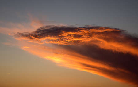 Cloud forming a wave shape and illuminated by the sun at sunset with red and gold colors